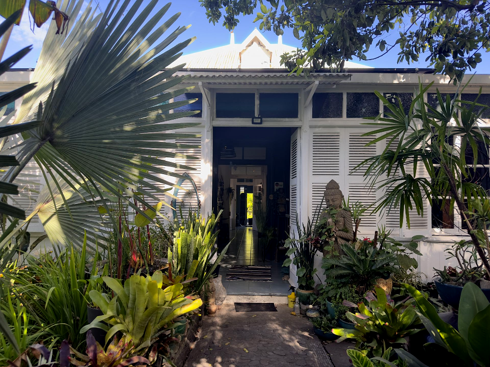 Façade blanche de la maison coloniale abritant la galerie La Villa Cachée, jardin tropical et statue de Bouddha à Nouméa