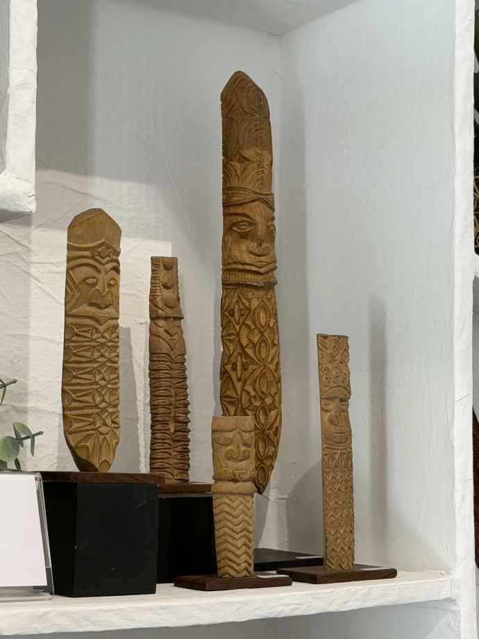Cinq sculptures kanak en bois aux motifs géométriques variés (étoiles, chevrons, losanges) exposées sur étagère