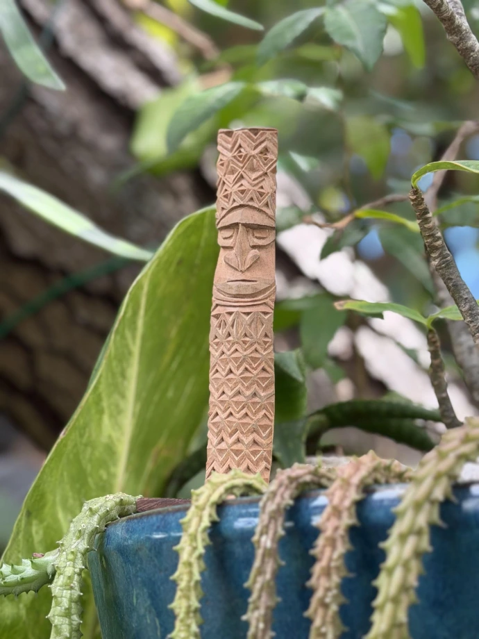 Sculpture kanak en bois à motifs chevronnés et losangiques, visage sculpté, posée près d'un pot bleu