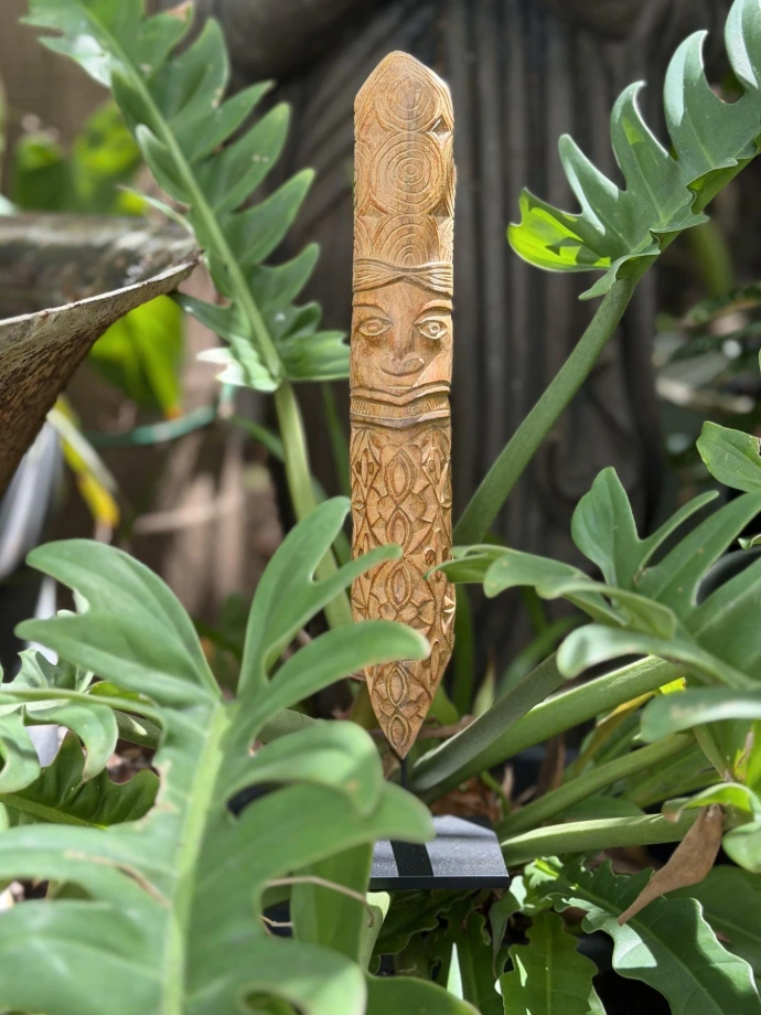 Sculpture kanak en bois à coiffe de cercles concentriques et corps à motifs en amande, œuvre d'Hervé Brukoa parmi les fougères