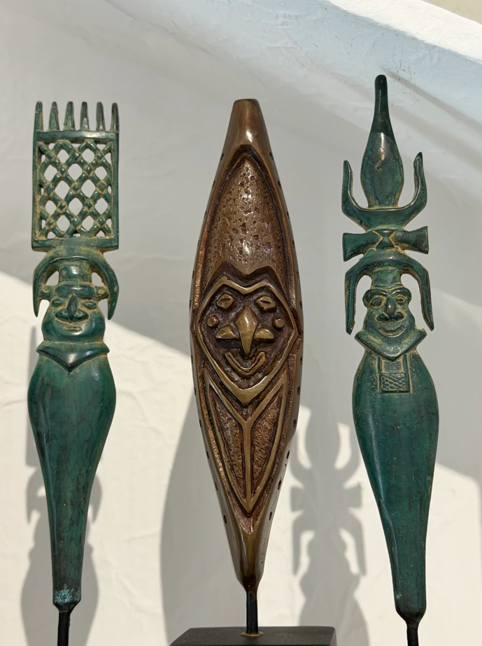 Trois flèches faîtières décoratives à patine verte et bronze, chacune ornée d'un visage sculpté