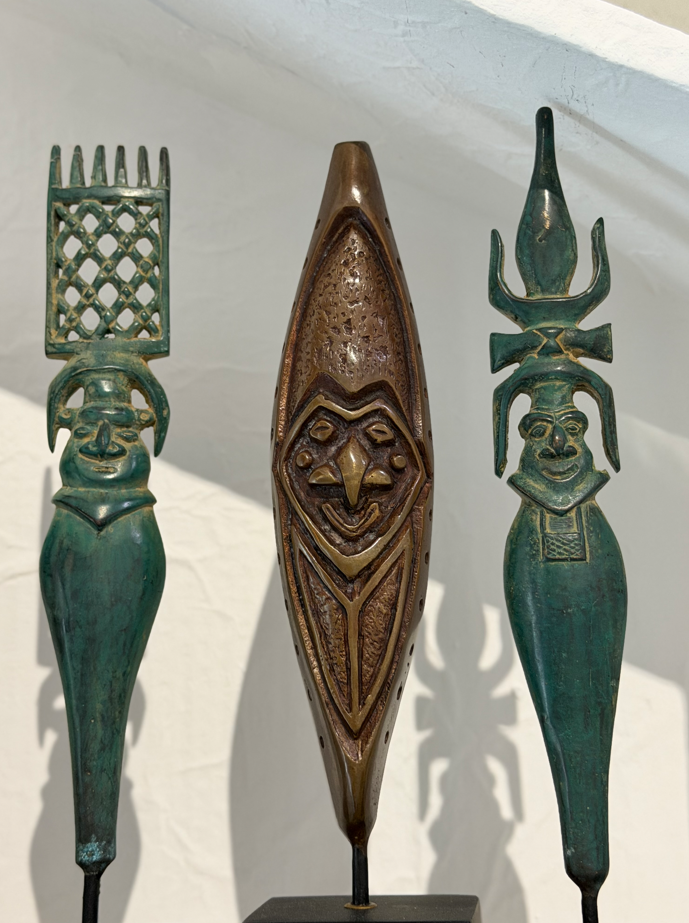 Trois flèches faîtières décoratives à patine verte et bronze, chacune ornée d'un visage sculpté