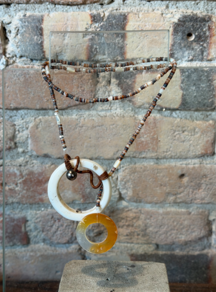 Collier en perles brunes et beiges orné de deux pendentifs ronds en nacre blanche et résine ambrée