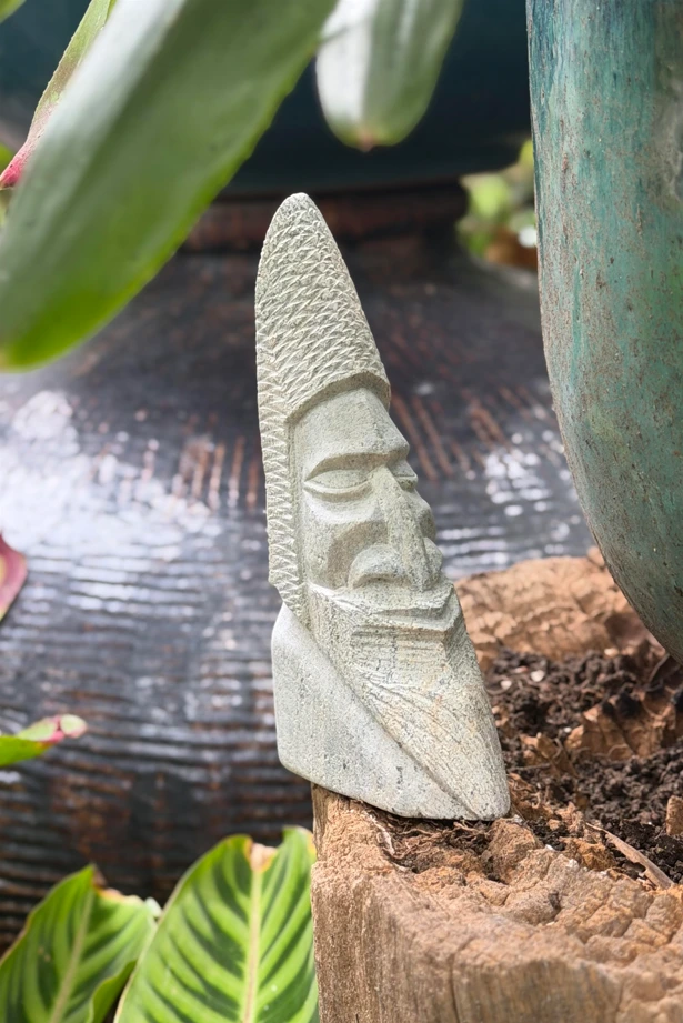 Sculpture en pierre à savon à coiffe conique quadrillée et visage barbu anguleux, posée dans le jardin de la Villa Cachée