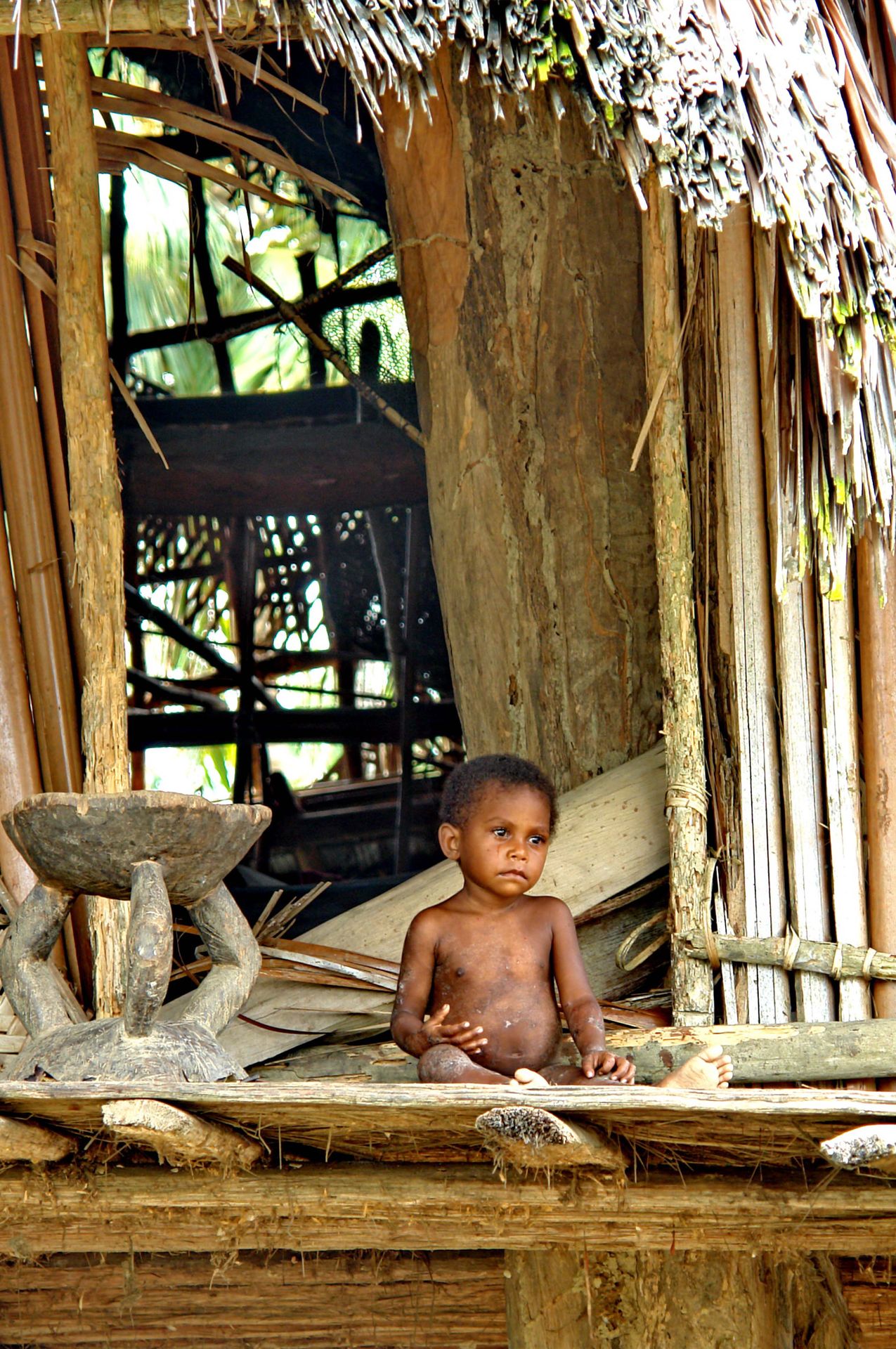 Enfant devant une habitation traditionnelle en Papouasie-Nouvelle-Guinée