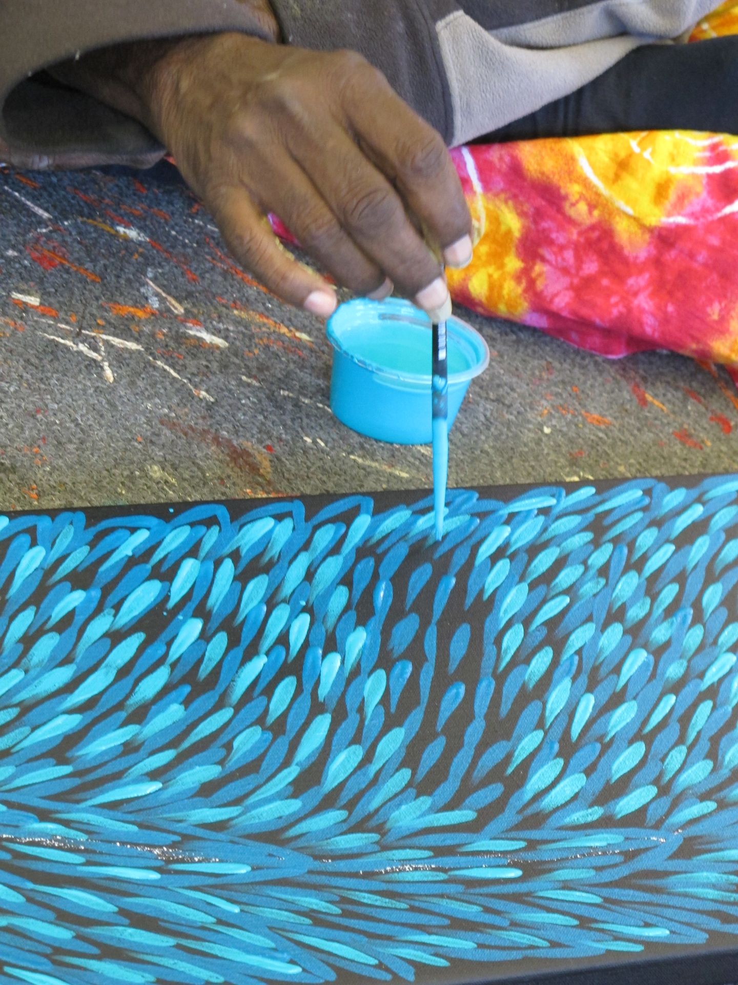 Main d'artiste aborigène peignant une œuvre de Gloria Petyarre, motifs de feuilles bleues style Bush Medicine Leaves