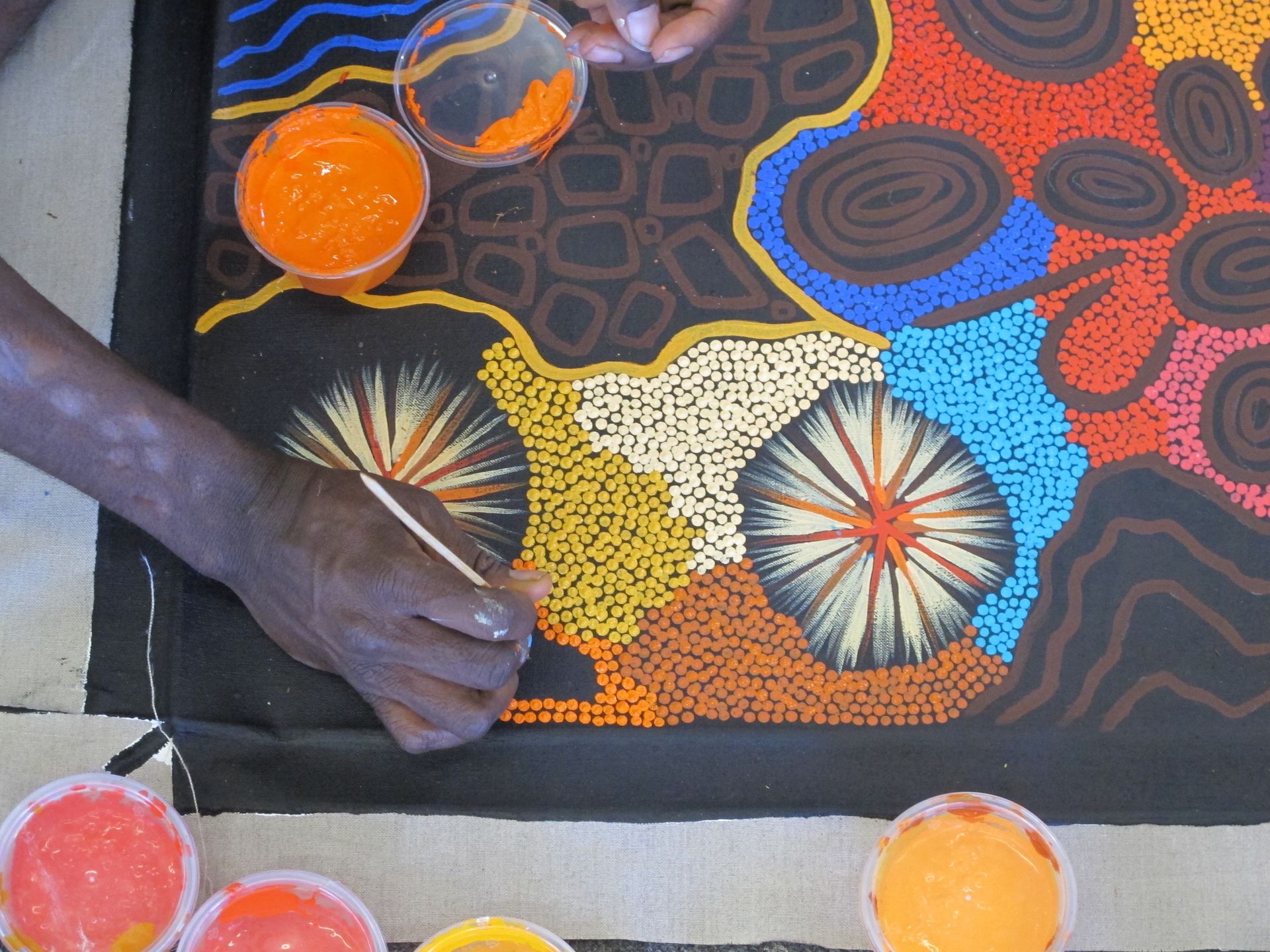 Main d'artiste aborigène peignant une œuvre de Yilpi Marcs, cercles concentriques colorés en technique du pointillisme