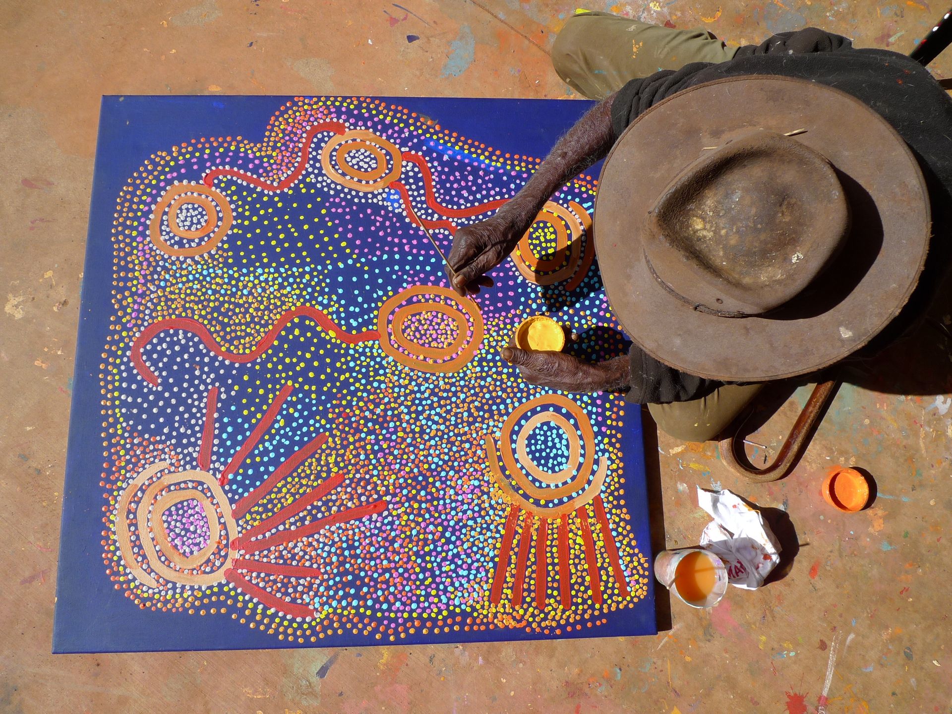 L'artiste aborigène Shorty Jangala peignant une œuvre en pointillisme, cercles concentriques orange sur fond bleu nuit