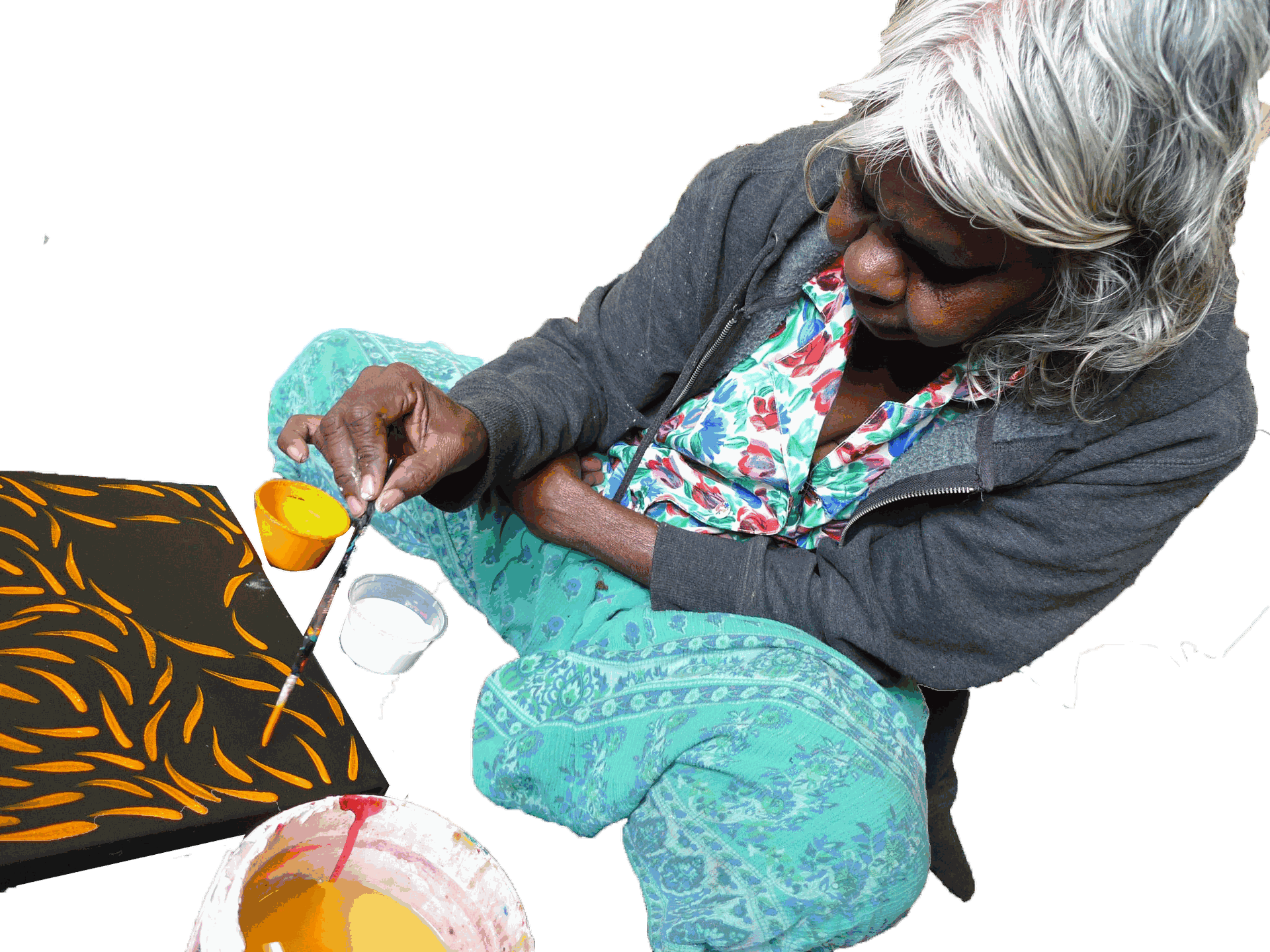 L'artiste aborigène Rosemary Pitjara peignant assise au sol une toile noire aux motifs d'herbes graines orange