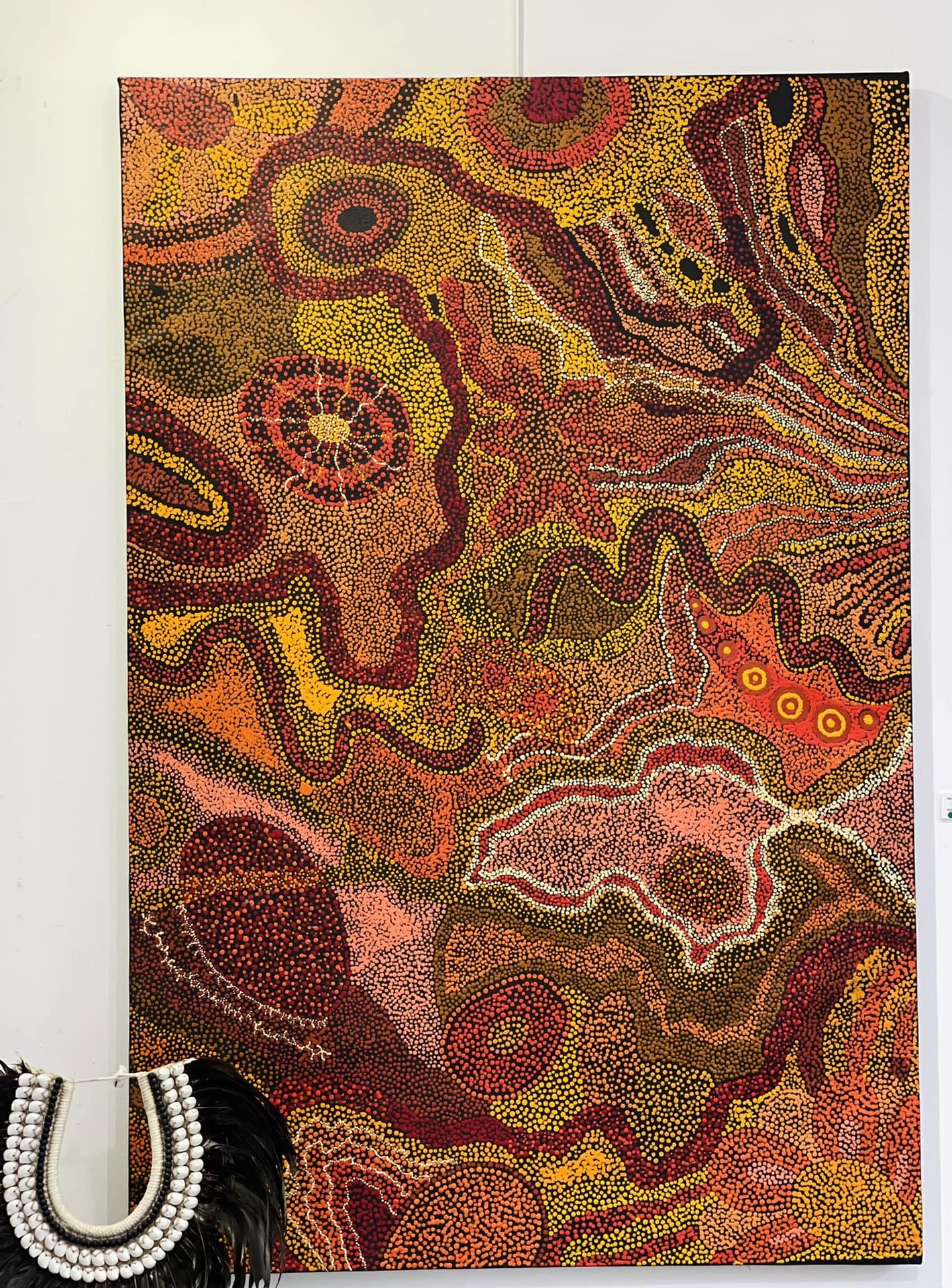 Grande toile d'art aborigène en pointillisme aux tons terre orange, rouge et jaune, exposée à la galerie La Villa Cachée
