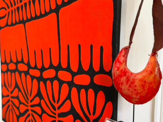 Toile aborigène rouge et noire aux motifs de feuilles et pointillés, accrochée près d'une gourde en cuir suspendue, exposition Rouge la Terre en Héritage