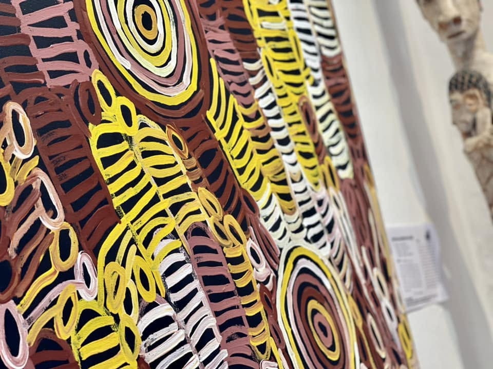 Détail d'une toile de Charmaine Pwerle aux cercles concentriques jaune et bordeaux reliés par des lignes striées, style Awelye
